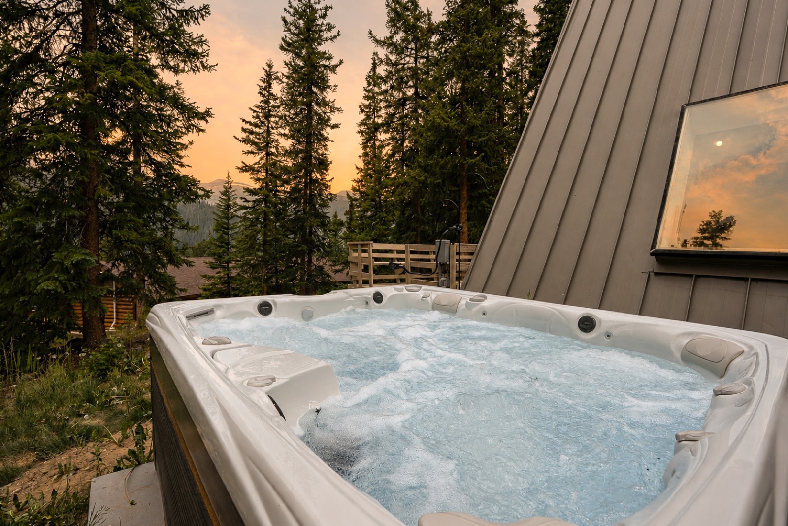 Bubbling hot tub beside an A-frame cabin at sunset in the pines