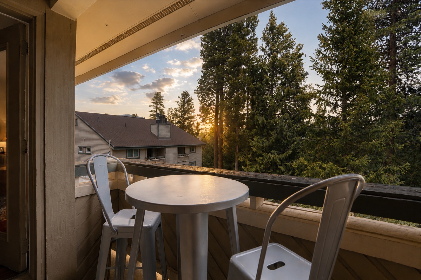 Balcony bistro table and chairs at sunset with forest and rooftops beyond