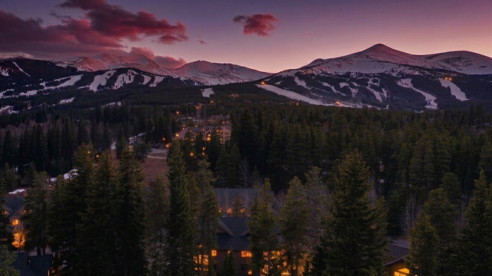 Breckenridge ski runs at twilight under a purple sky with forested slopes below