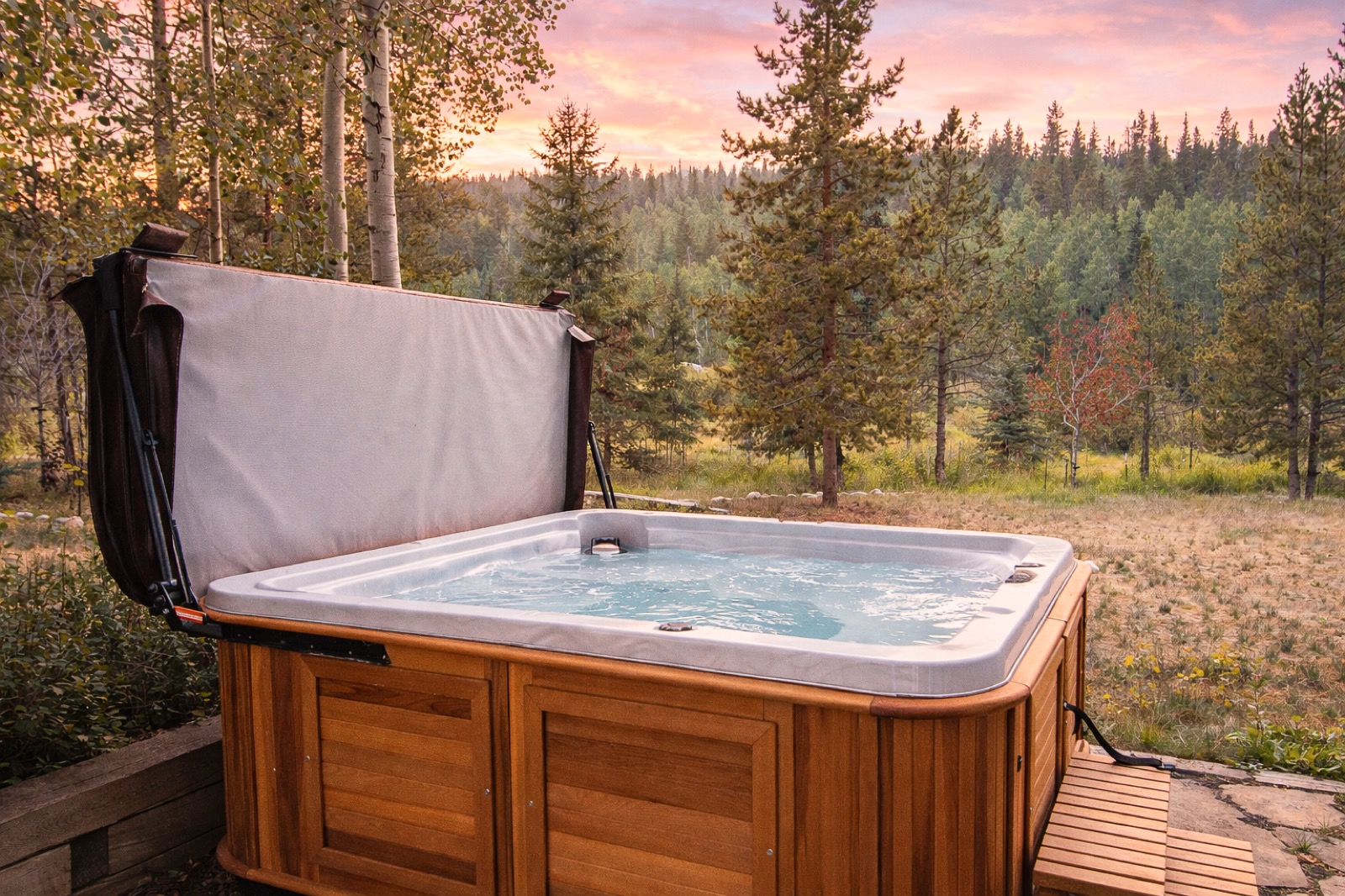 Cedar hot tub at sunset overlooking a mountain meadow under a pink and purple sky