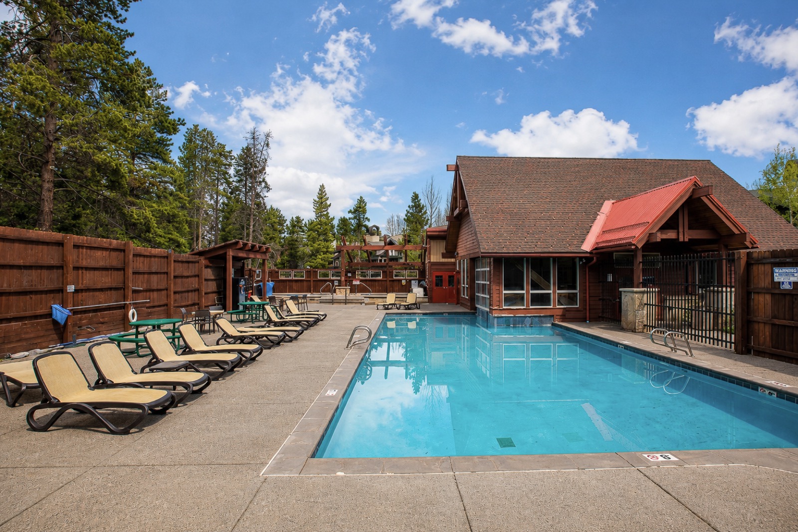 Outdoor community pool with lounge chairs beside a timber clubhouse