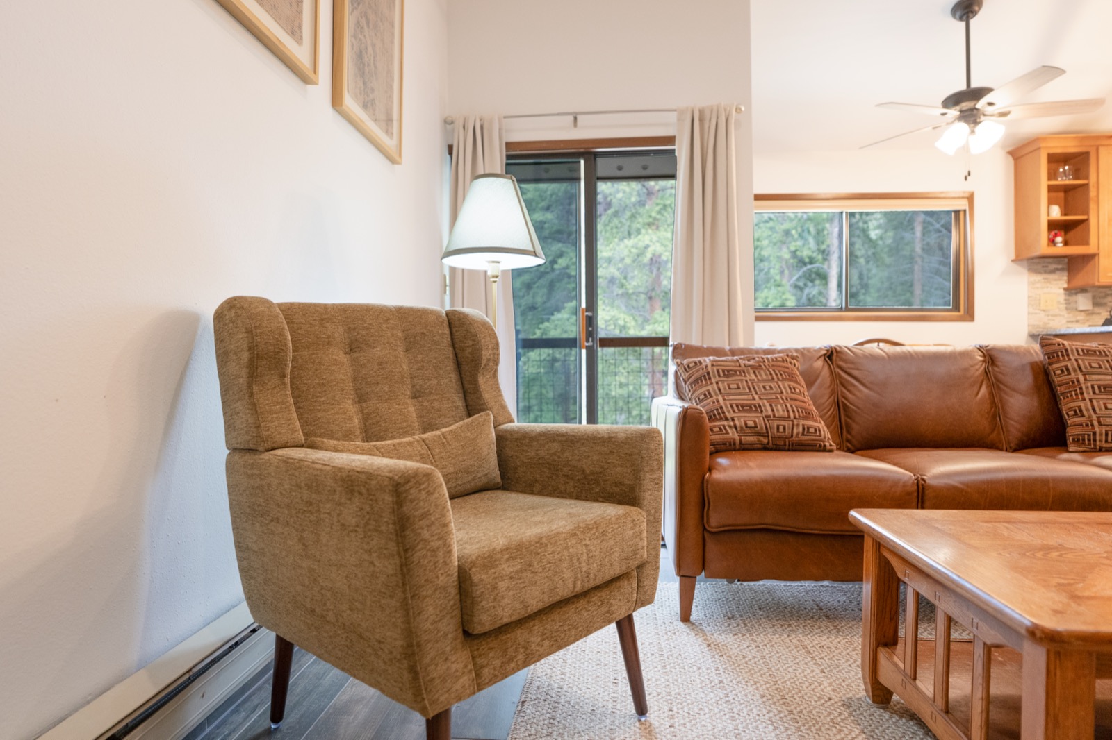 Bright condo living room with leather sofa, armchair, and forest views through the windows