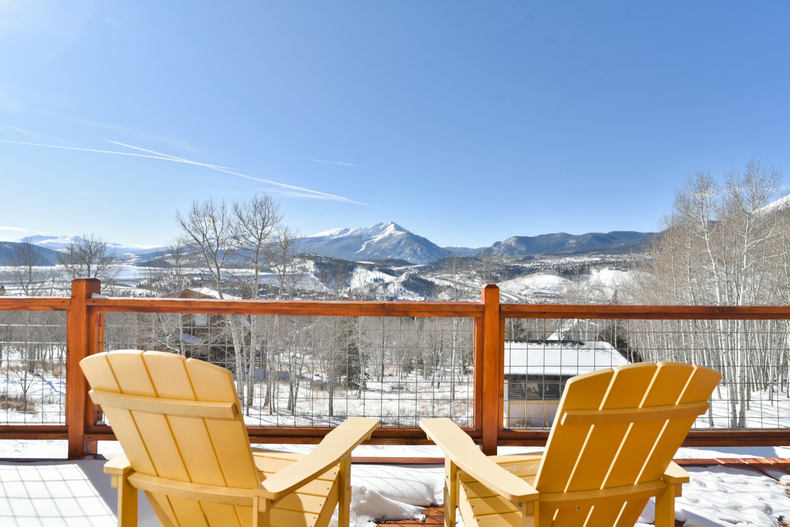 Yellow Adirondack chairs on a snowy deck overlooking Colorado mountain peaks under a blue sky