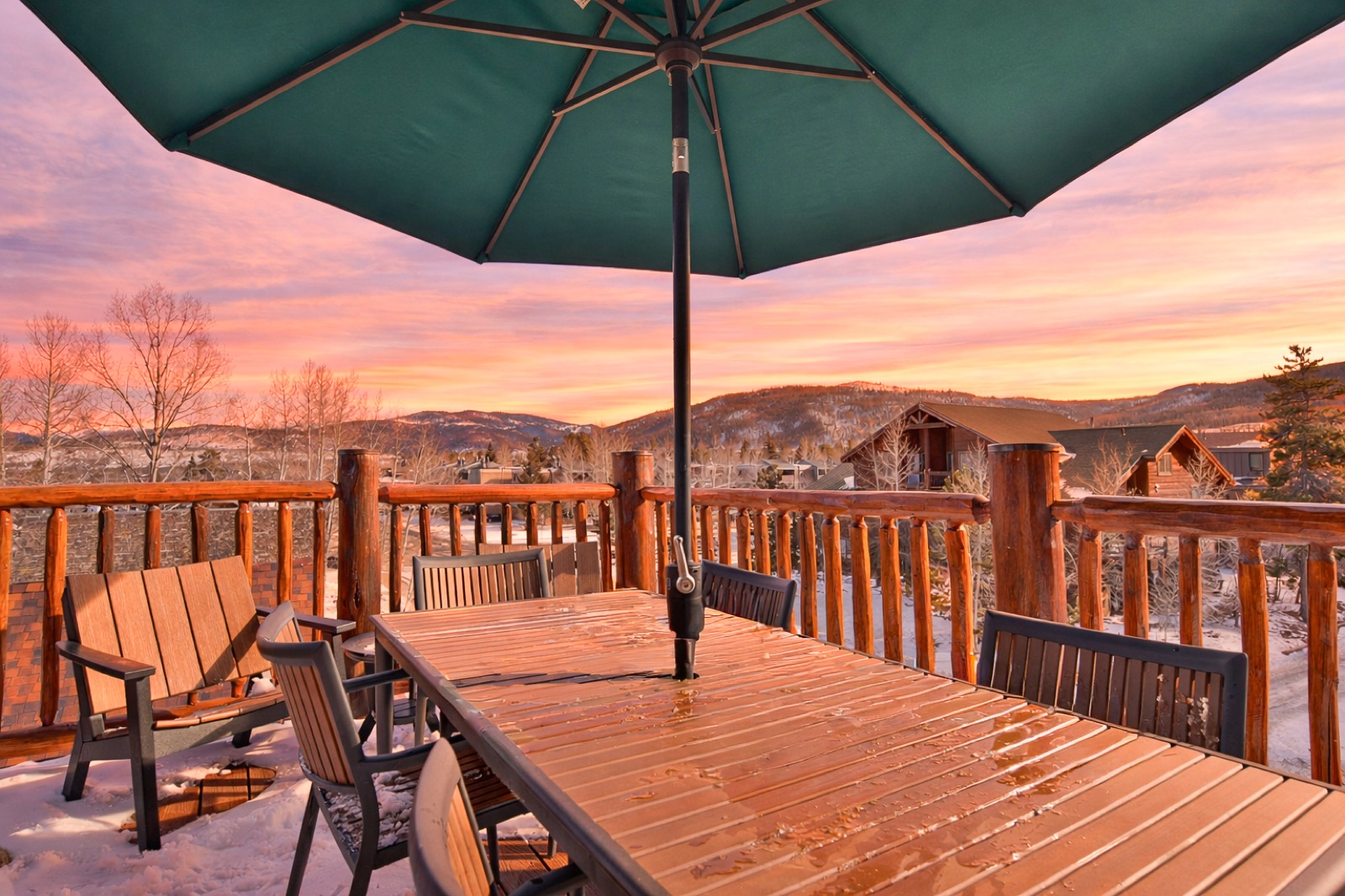 Log-railing deck with patio table and green umbrella at sunset over mountain rooftops