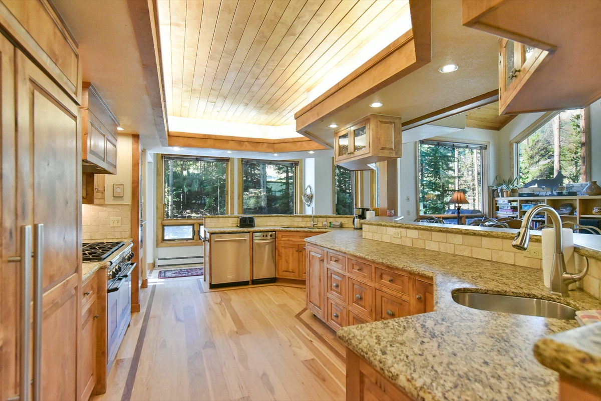 Bright mountain home kitchen with wood plank ceiling, granite counters, and forest views through the windows