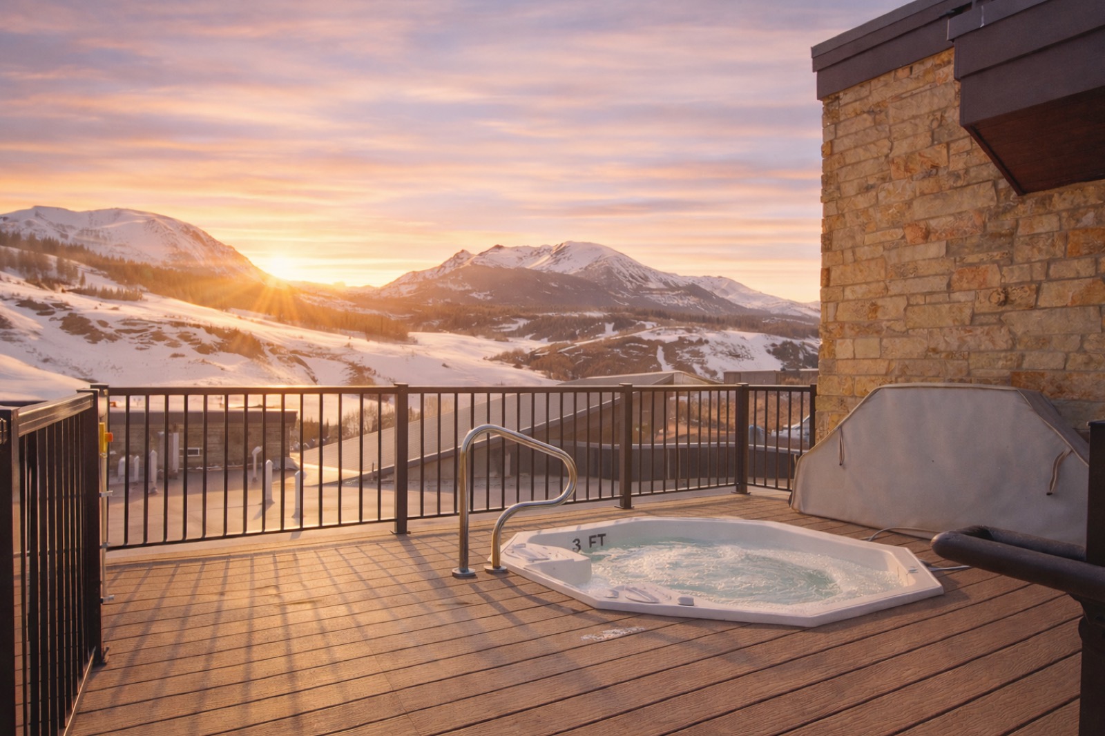 Rooftop hot tub at sunset overlooking snowy mountain peaks and a stone chimney